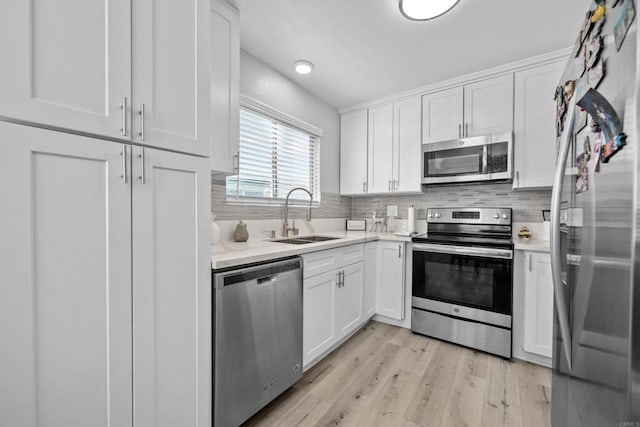 kitchen with appliances with stainless steel finishes, light hardwood / wood-style flooring, white cabinetry, and sink