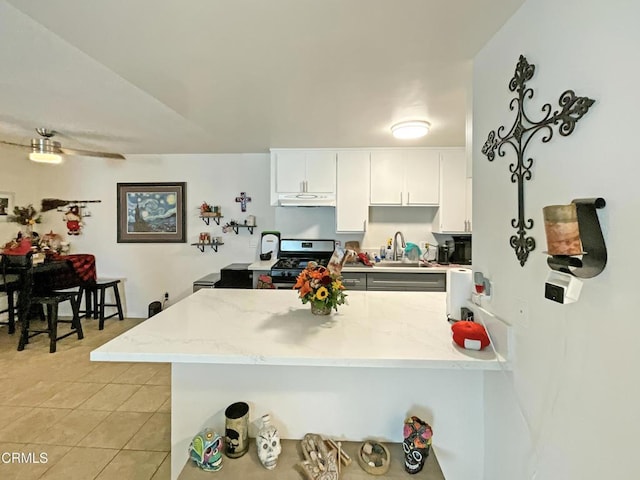 kitchen featuring kitchen peninsula, sink, light tile patterned flooring, white cabinetry, and stainless steel gas stove