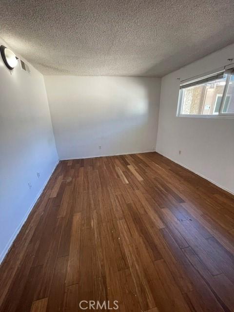 empty room with dark wood-type flooring and a textured ceiling