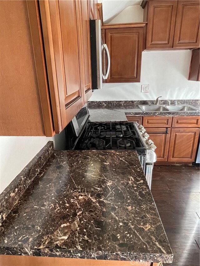 kitchen with stainless steel appliances, sink, dark stone countertops, and dark hardwood / wood-style floors