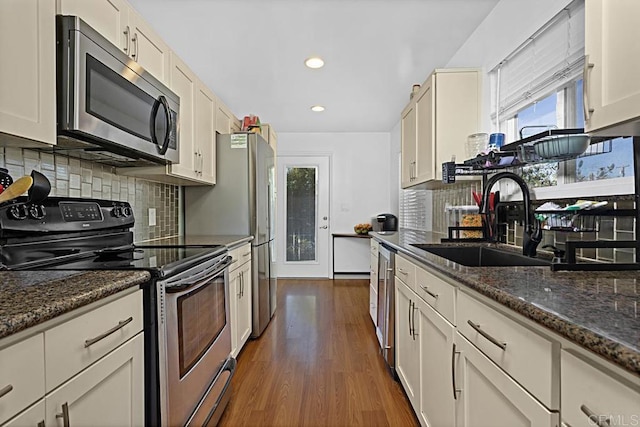 kitchen featuring sink, appliances with stainless steel finishes, dark stone countertops, tasteful backsplash, and dark hardwood / wood-style flooring