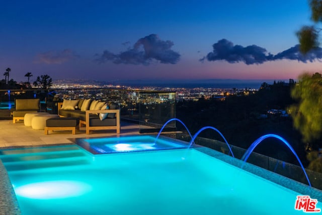 pool at dusk with an in ground hot tub, outdoor lounge area, pool water feature, and a patio area