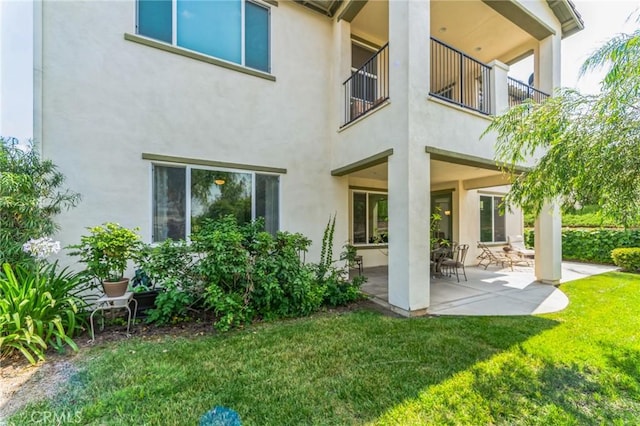 rear view of property featuring a patio area, a balcony, and a yard