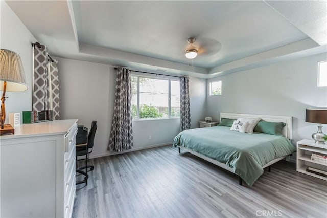 bedroom with ceiling fan, a raised ceiling, and light wood-type flooring