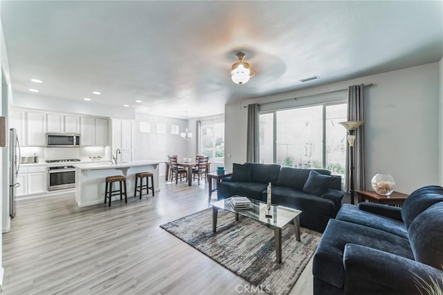 living room with ceiling fan with notable chandelier and light wood-type flooring