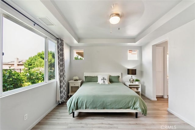 bedroom with a raised ceiling, ceiling fan, and light hardwood / wood-style flooring