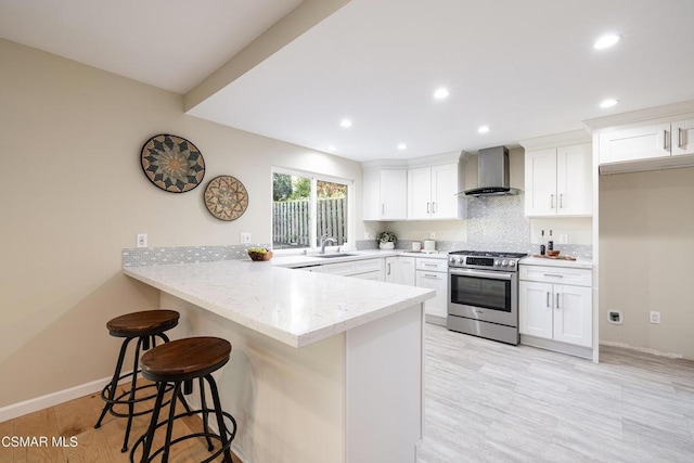 kitchen with stainless steel range, a kitchen breakfast bar, white cabinets, and wall chimney exhaust hood