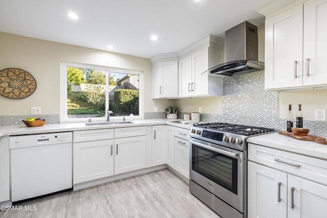 kitchen featuring dishwasher, high end range, sink, wall chimney exhaust hood, and white cabinetry