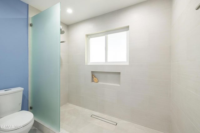 bathroom featuring tile patterned flooring, toilet, and tiled shower