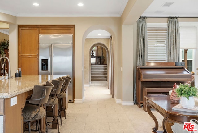 interior space with light stone countertops, sink, stainless steel built in fridge, a breakfast bar, and ornamental molding