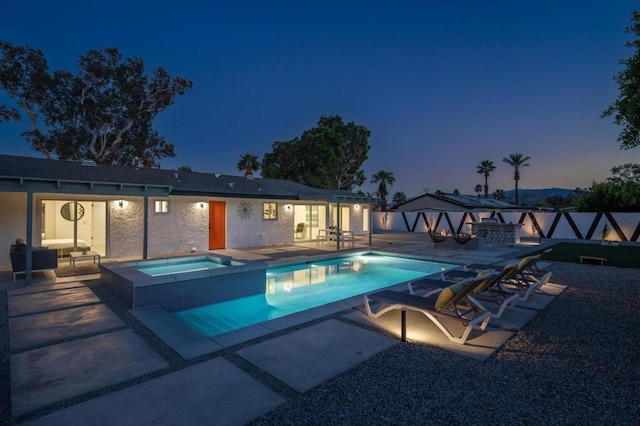 pool at dusk featuring a patio area and an in ground hot tub