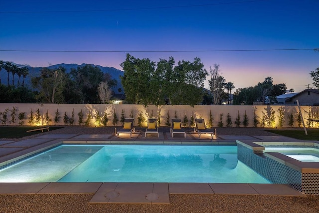 pool at dusk with an in ground hot tub and a mountain view