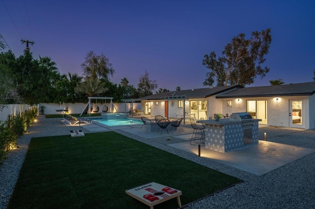 back house at dusk with an outdoor kitchen and a patio