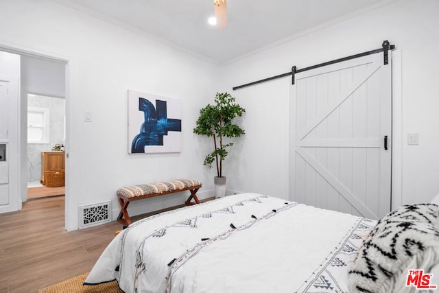 bedroom featuring a barn door, light hardwood / wood-style floors, and ornamental molding