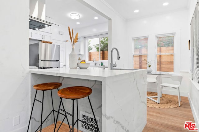 kitchen featuring stainless steel refrigerator, sink, light hardwood / wood-style floors, extractor fan, and white cabinets