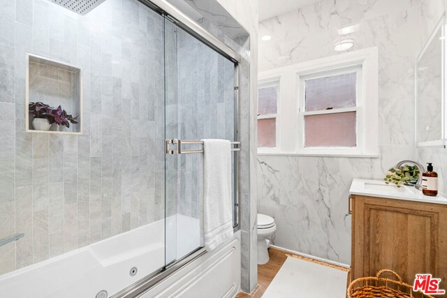 full bathroom with vanity, combined bath / shower with glass door, hardwood / wood-style flooring, toilet, and tile walls