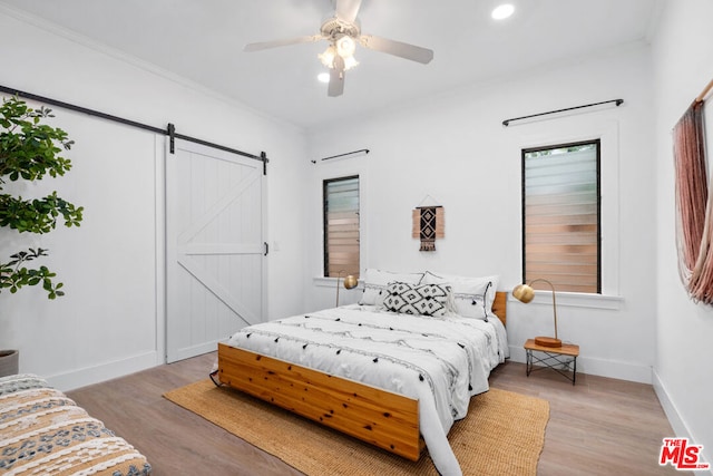 bedroom featuring a barn door, ceiling fan, crown molding, and light wood-type flooring