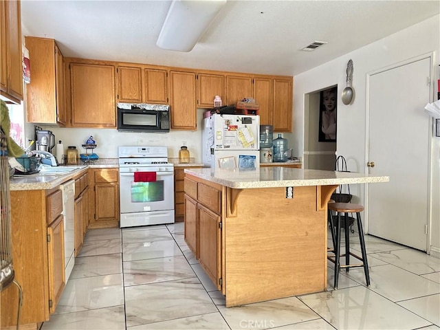 kitchen with a breakfast bar area, a kitchen island, sink, and white appliances