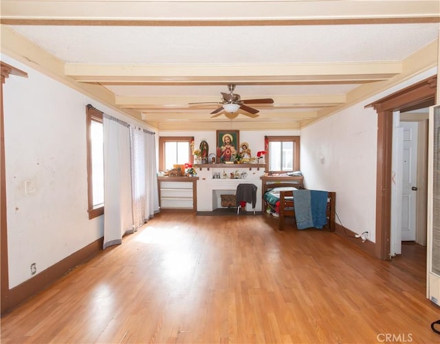 unfurnished living room with beamed ceiling, ceiling fan, a healthy amount of sunlight, and light wood-type flooring