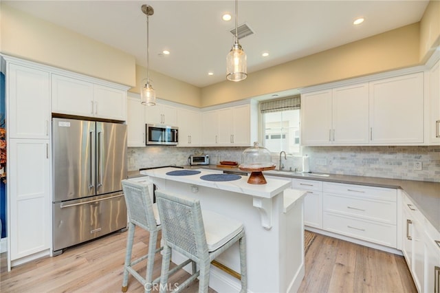 kitchen featuring stainless steel appliances, a kitchen island, light hardwood / wood-style flooring, pendant lighting, and white cabinets