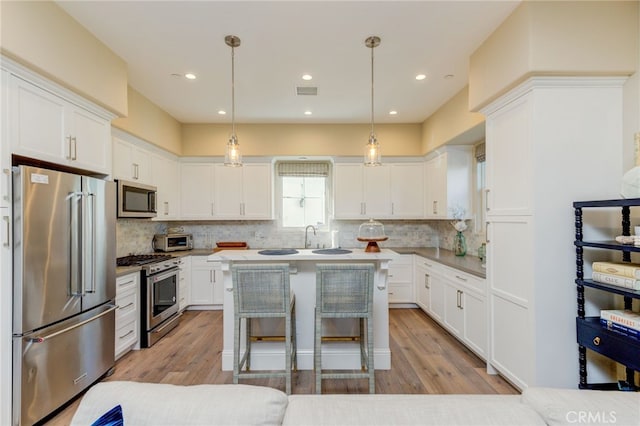 kitchen featuring pendant lighting, a kitchen breakfast bar, light hardwood / wood-style flooring, appliances with stainless steel finishes, and white cabinetry