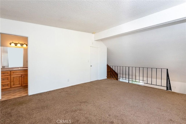 unfurnished room featuring sink, a textured ceiling, lofted ceiling with beams, and carpet flooring