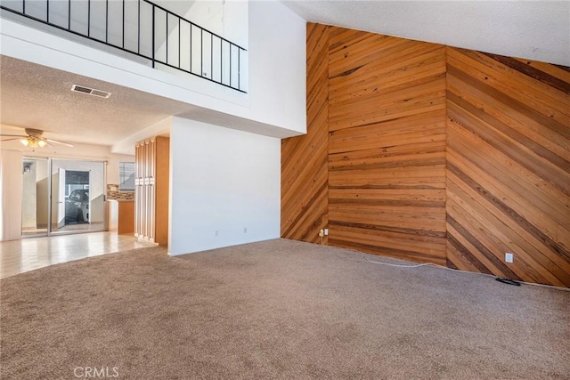 unfurnished living room with a high ceiling, a textured ceiling, wood walls, carpet flooring, and ceiling fan