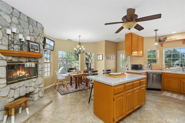 kitchen featuring tile countertops, a stone fireplace, decorative light fixtures, dishwasher, and a center island