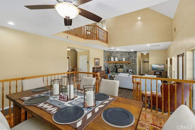 dining area with a high ceiling, ceiling fan, a fireplace, and hardwood / wood-style floors