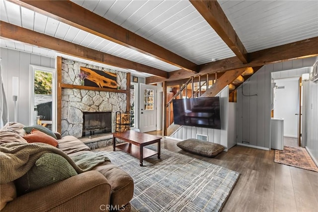 living room with dark hardwood / wood-style flooring, a stone fireplace, and beam ceiling