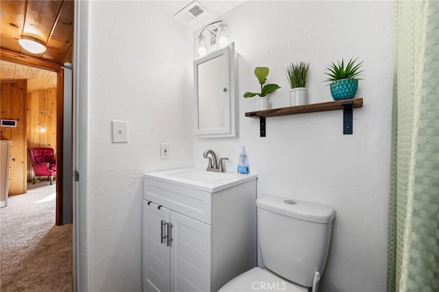 bathroom featuring vanity, wooden walls, and toilet