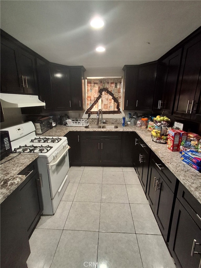 kitchen featuring white range with gas stovetop, light tile patterned floors, light stone counters, and sink