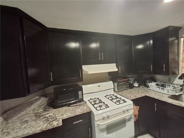 6100 Rugby Ave Unit 207, Huntington Park, CA 90255 - kitchen with under cabinet range hood, white gas range, dark cabinetry, and light stone countertops