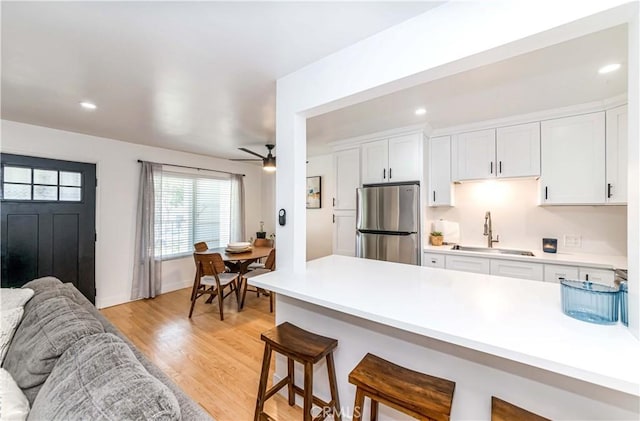 kitchen featuring white cabinets, light wood-type flooring, sink, and stainless steel refrigerator