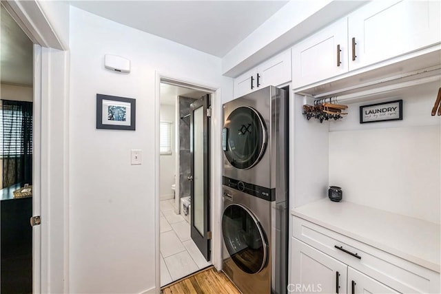 laundry room with light hardwood / wood-style floors, cabinets, and stacked washer / dryer