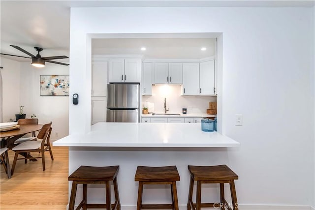 kitchen with white cabinets, a kitchen breakfast bar, ceiling fan, light hardwood / wood-style floors, and stainless steel refrigerator