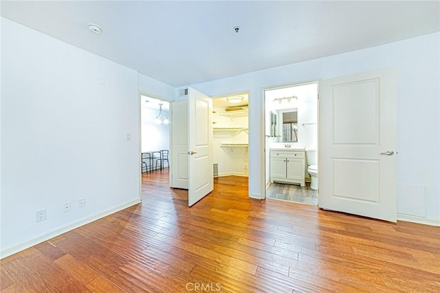 unfurnished bedroom featuring ensuite bath, a spacious closet, a chandelier, light hardwood / wood-style floors, and a closet