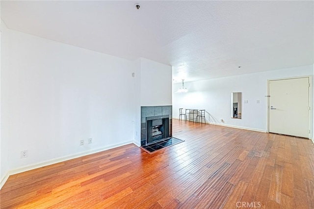 unfurnished living room featuring a notable chandelier, wood-type flooring, and a tiled fireplace