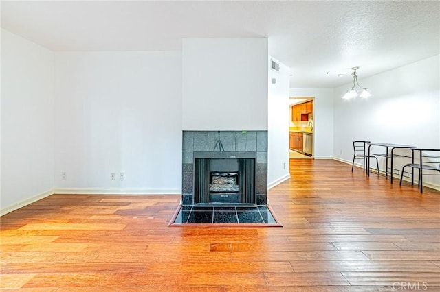 living room with a tiled fireplace, hardwood / wood-style floors, a chandelier, and a textured ceiling