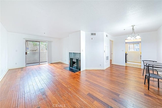 living room featuring wood-type flooring, a textured ceiling, a notable chandelier, and a tiled fireplace