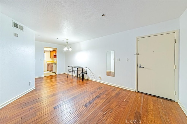 unfurnished room with hardwood / wood-style flooring, a textured ceiling, and an inviting chandelier