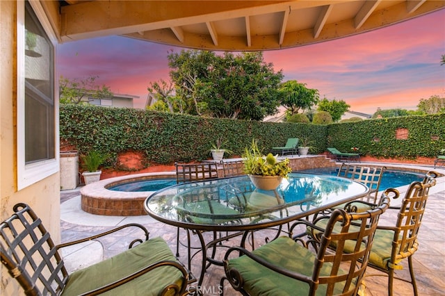 pool at dusk with a patio area and an in ground hot tub