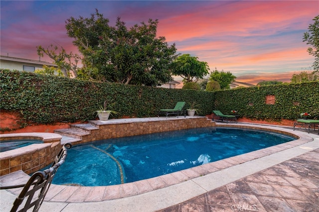 pool at dusk featuring an in ground hot tub