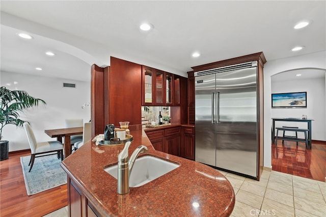 kitchen with light hardwood / wood-style flooring, built in refrigerator, dark stone counters, and sink