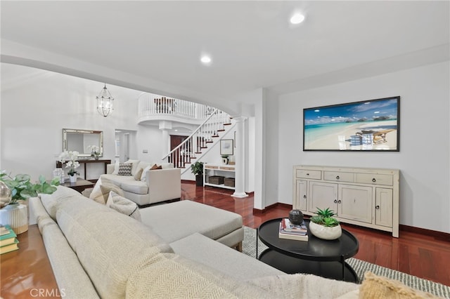 living room featuring ornate columns, dark wood-type flooring, and a notable chandelier