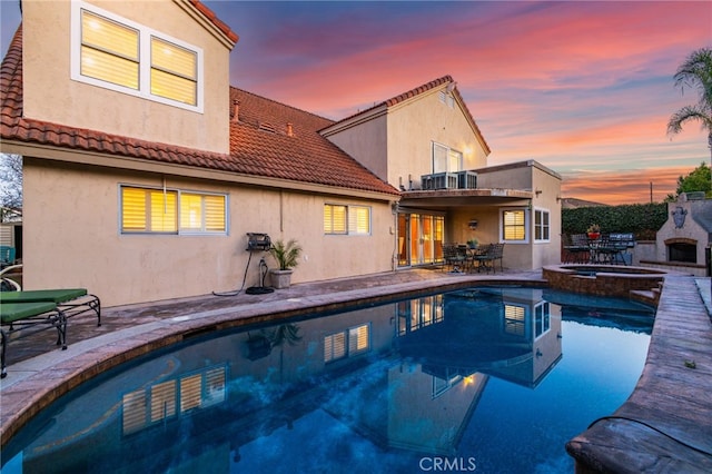 pool at dusk with an in ground hot tub, a patio, and exterior fireplace