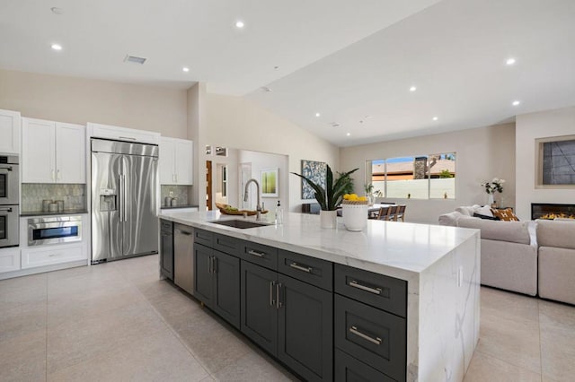 kitchen with lofted ceiling, backsplash, sink, an island with sink, and stainless steel appliances