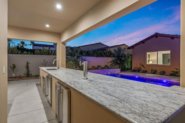 patio terrace at dusk with pool water feature, a fenced in pool, beverage cooler, and an outdoor wet bar