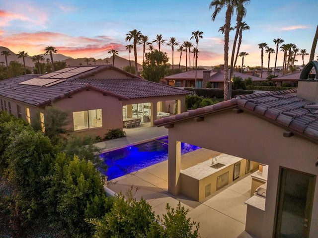 pool at dusk featuring exterior kitchen and a patio