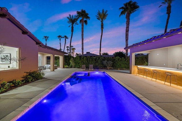 pool at dusk featuring a patio area and exterior bar